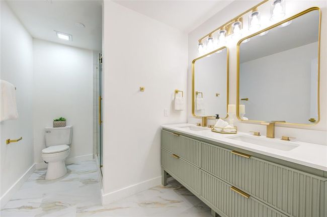 The primary bathroom has been fully renovated with new tile floors, a walk-in shower with a modern glass door, and a double vanity with Quartz countertops. The sleek design and updated fixtures add a spa-like feel to the space. | Image 18