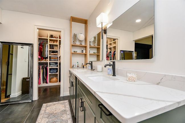 This photo showcases a modern bathroom with dual sinks, sleek fixtures, and a large mirror. Adjacent is a spacious walk-in closet with ample shelving and storage space. The design is clean and stylish, ideal for a homebuyer seeking convenience and elegance. | Image 29