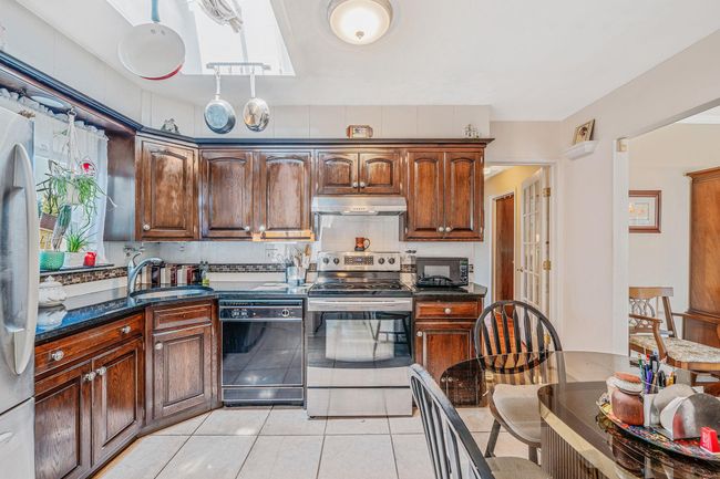 Kitchen with black appliances, under cabinet range hood, light tile patterned floors, and dark stone countertops | Image 11