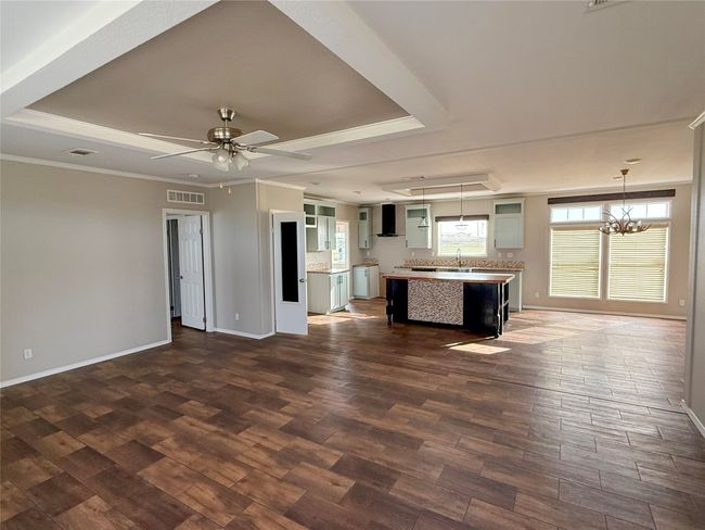 Unfurnished living room with a tray ceiling, ceiling fan, dark wood finished floors, crown molding, and a chandelier | Image 7