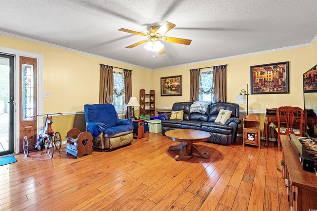 Living room with light wood-style flooring, ceiling fan, a textured ceiling, plenty of natural light, and ornamental molding | Image 8