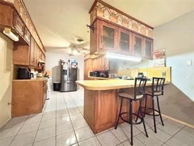 Kitchen with light tile patterned floors, a peninsula, glass insert cabinets, and brown cabinets | Image 6