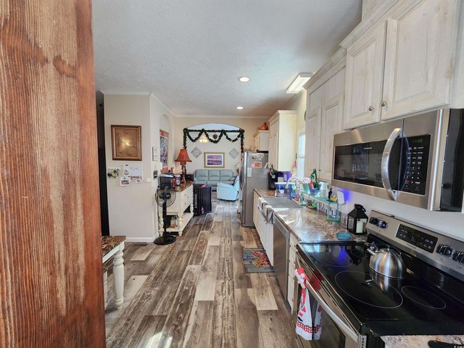 Kitchen with hardwood / wood-style flooring, ornamental molding, a textured ceiling, appliances with stainless steel finishes, and white cabinetry | Image 13