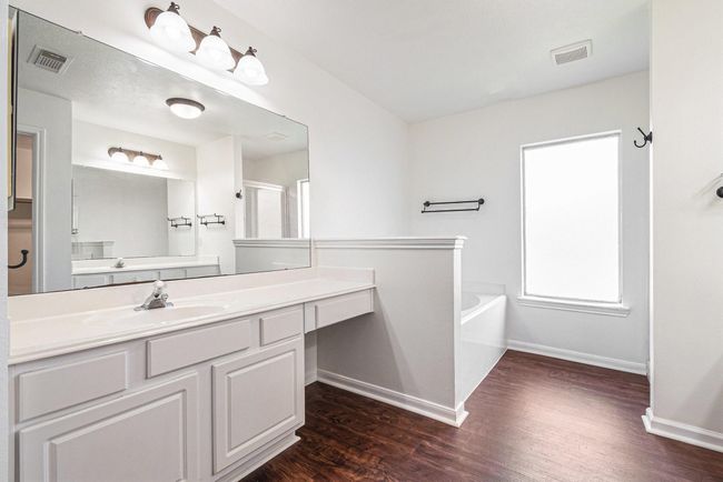 Bright, spacious bathroom with a large mirror, dual sinks, separate bathtub and shower. Features modern lighting and vinyl wood-look flooring, creating a clean, elegant feel. | Image 10