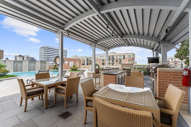 This photo showcases a modern outdoor area, featuring a covered seating area with wicker furniture, a grill, and a pool with cityscape views in the background. Ideal for relaxation and entertaining. | Image 28