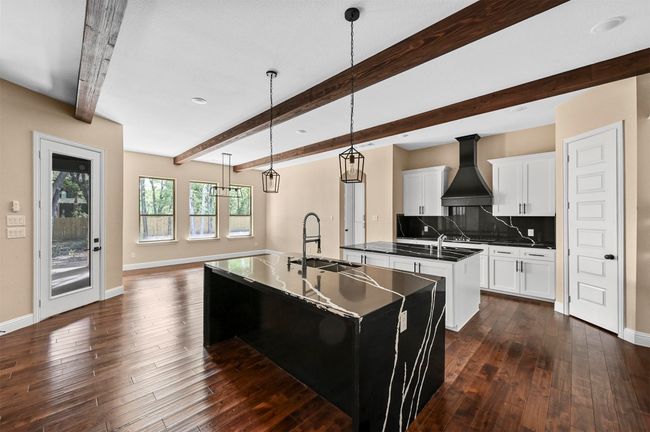 Kitchen with dark wood-style flooring, custom exhaust hood, decorative backsplash, a sink, and an island with sink | Image 23