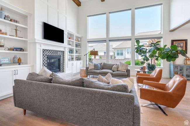 Living area with healthy amount of natural light, light wood-style flooring, a tile fireplace, a towering ceiling, and built in shelves | Image 8