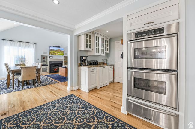 Kitchen with light wood finished floors, ornamental molding, a lit fireplace, stainless steel double oven, and a warming drawer | Image 10