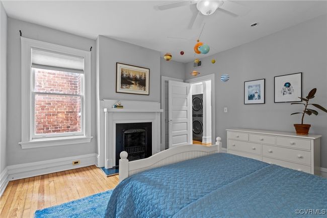 Bedroom featuring a fireplace with raised hearth, ceiling fan, light wood finished floors, baseboards, and stacked washer and clothes dryer | Image 25