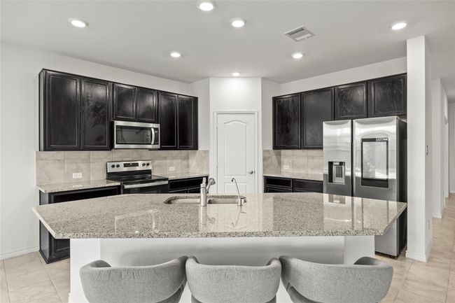 Kitchen with appliances with stainless steel finishes, dark cabinets, a sink, light stone counters, and recessed lighting | Image 13