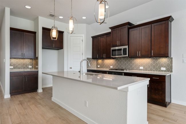 Kitchen featuring stainless steel appliances, tasteful backsplash, light wood-style floors, a center island with sink, and dark brown cabinets, oversized kitchen pantry | Image 11