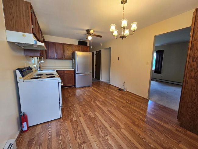 Kitchen with white appliances, a baseboard heating unit, a sink, a ceiling fan, and wood finished floors | Image 13