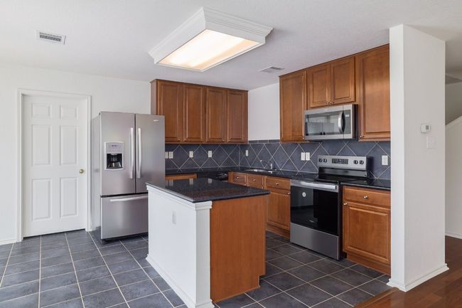Kitchen with brown cabinets, a center island, visible vents, and appliances with stainless steel finishes | Image 12