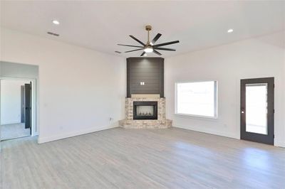 Unfurnished living room featuring a large fireplace, ceiling fan, and light hardwood / wood-style floors | Image 2