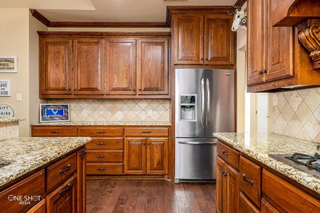 Kitchen with appliances with stainless steel finishes, backsplash, crown molding, light stone counters, and dark wood-style flooring | Image 17