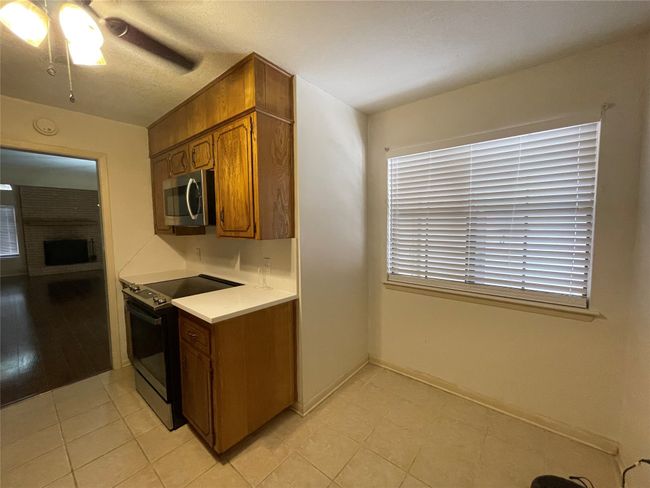 Kitchen featuring range with electric stovetop, stainless steel microwave, light countertops, brown cabinetry, and light tile patterned floors | Image 13