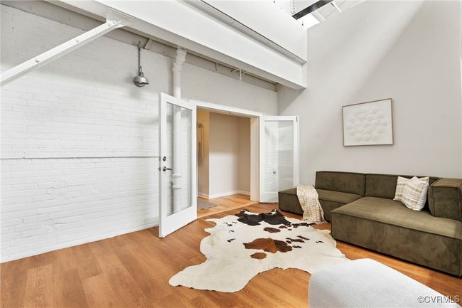 Living area featuring brick wall, a high ceiling, french doors, and wood finished floors | Image 21