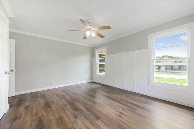 Empty room featuring ceiling fan, healthy amount of natural light, dark wood-style flooring, ornamental molding, and a decorative wall | Image 27