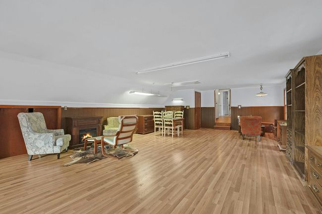 Living area with wooden walls, wainscoting, light wood-style flooring, and a lit fireplace | Image 28