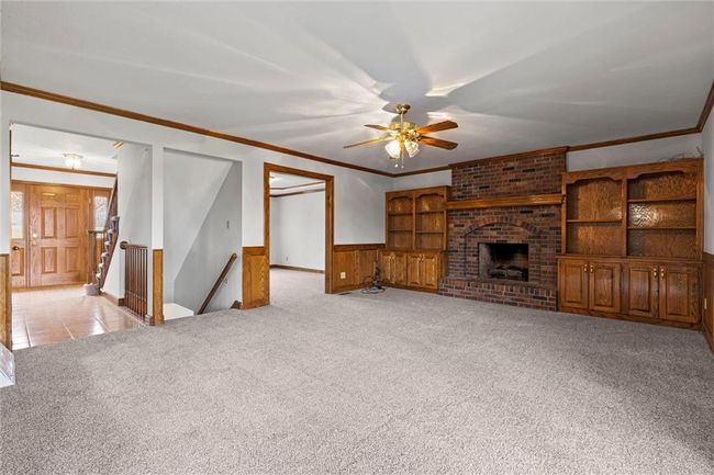 Unfurnished living room with ceiling fan, a brick fireplace, wooden walls, light carpet, and ornamental molding | Image 8