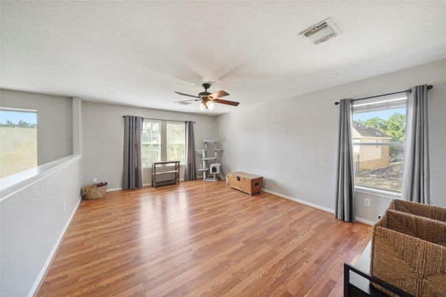 Spacious, bright gameroom with large windows, hardwood floors, and neutral walls. Features a ceiling fan, ample natural light. | Image 22