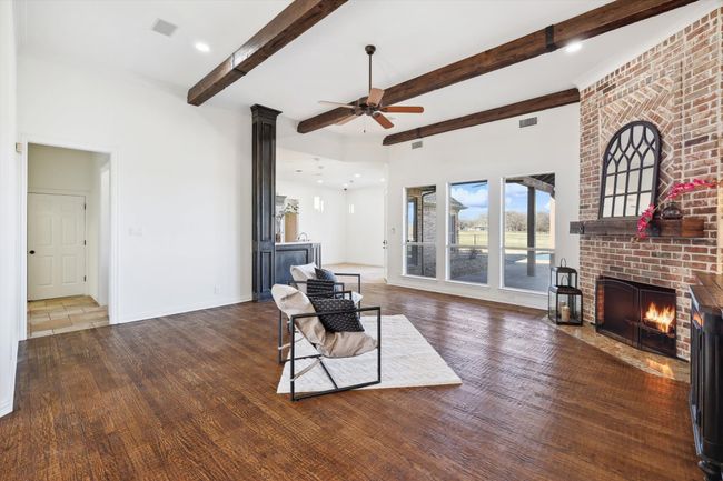 Living area featuring a ceiling fan, a brick fireplace, beamed ceiling, wood finished floors, and baseboards | Image 9