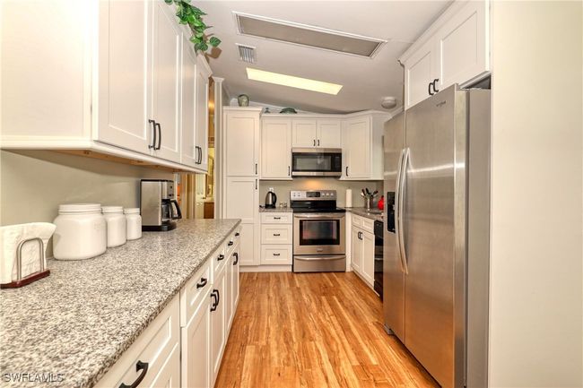 Kitchen with lofted ceiling, white cabinets, light hardwood / wood-style flooring, appliances with stainless steel finishes, and light stone counters | Image 7