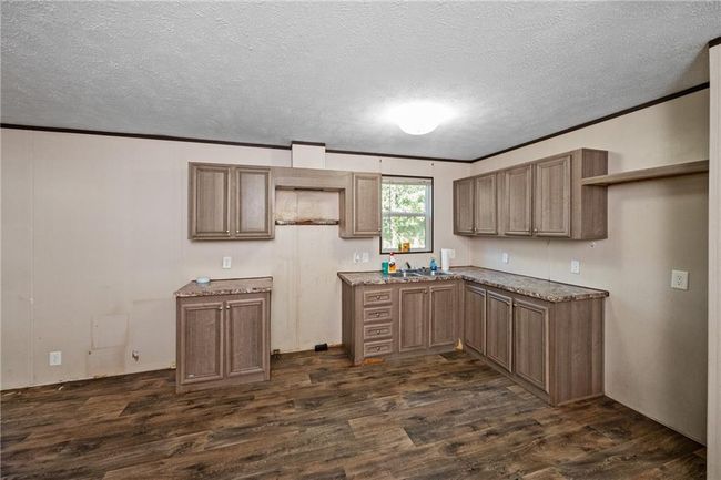 Kitchen featuring dark wood-style flooring, crown molding, a textured ceiling, a sink, and light stone counters | Image 16
