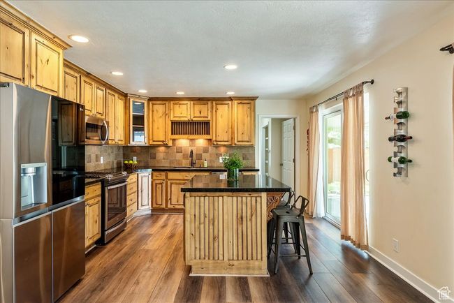 Kitchen featuring appliances with stainless steel finishes, dark wood-style floors, a center island, backsplash, and glass insert cabinets | Image 17