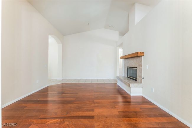 Unfurnished living room featuring wood finished floors, a tiled fireplace, vaulted ceiling, arched walkways, and baseboards | Image 22