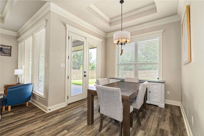 Bright breakfast area featuring rich dark wood floors, elegant crown molding, a tray ceiling, and a stunning chandelier. | Image 15