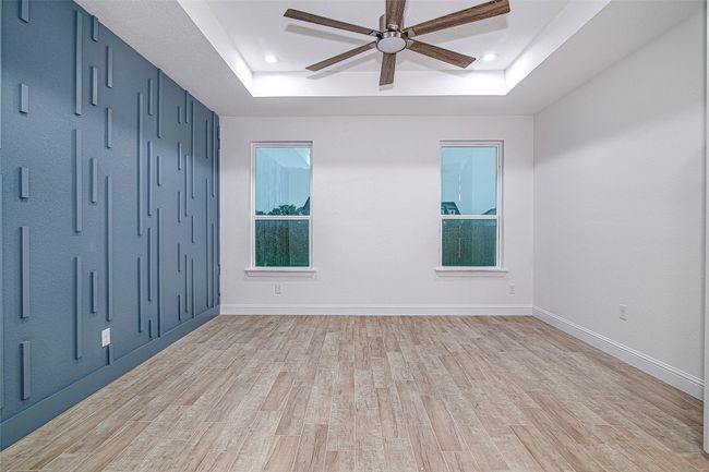 Empty room with a raised ceiling, a ceiling fan, light wood-type flooring, recessed lighting, and baseboards | Image 20