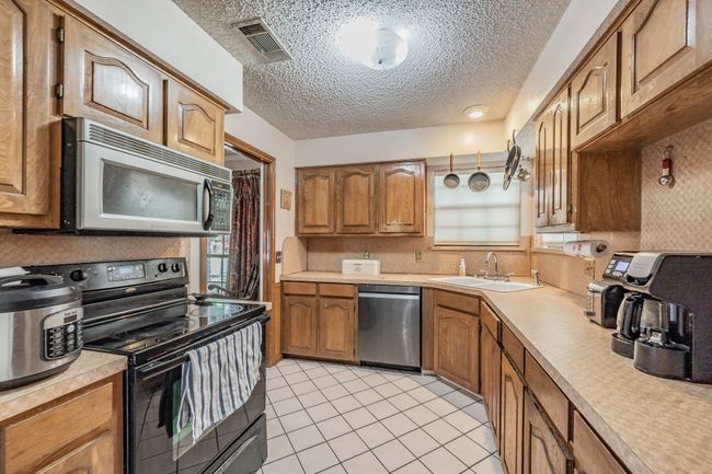 Kitchen with stainless steel appliances, light countertops, brown cabinets, light tile patterned flooring, and a textured ceiling | Image 10