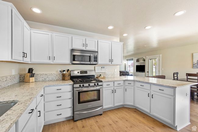 Kitchen featuring stainless steel appliances, a peninsula, white cabinetry, and light wood-style flooring | Image 11