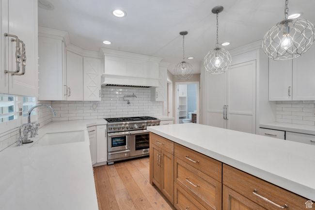 Kitchen featuring range with two ovens, custom exhaust hood, a sink, light countertops, and backsplash | Image 13