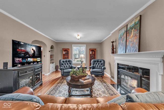 living area featuring a tile fireplace, baseboards, ornamental molding, built in shelves, and wood finished floors | Image 6