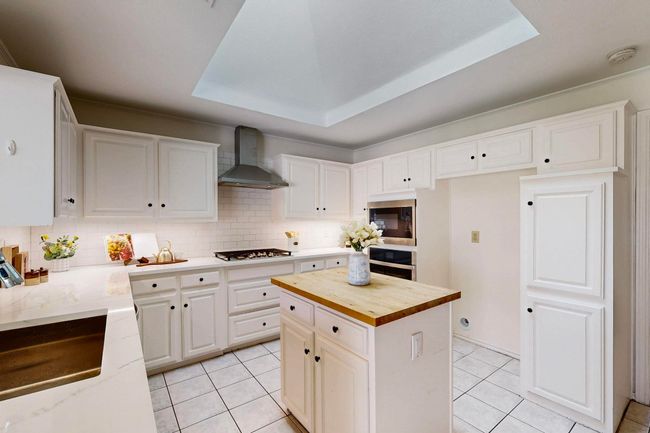 Kitchen with wood counters, light tile patterned flooring, white cabinetry, and wall chimney range hood | Image 10