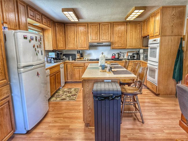Kitchen featuring white appliances, a center island, light countertops, under cabinet range hood, and light wood finished floors | Image 17