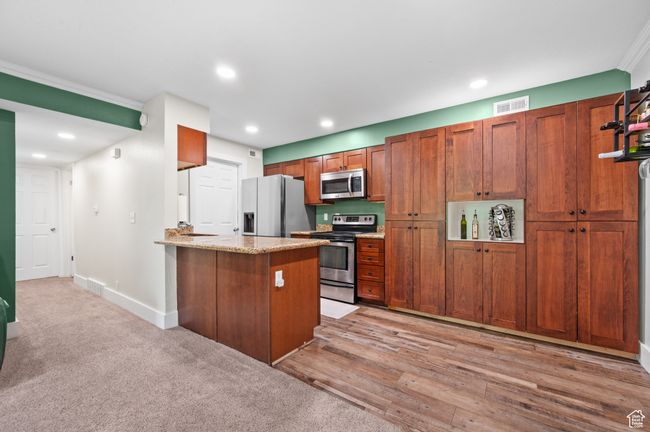 Kitchen with stainless steel appliances, a peninsula, recessed lighting, brown cabinetry, and light stone counters | Image 6