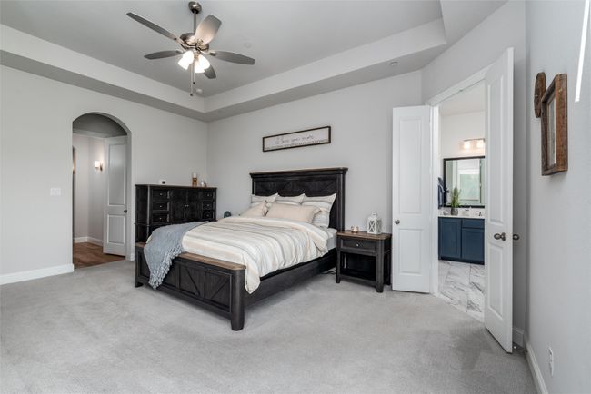 Bedroom with arched walkways, light carpet, baseboards, connected bathroom, and ceiling fan | Image 15