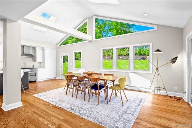 Dining room featuring baseboard heating, a skylight, light wood-type flooring, baseboards, and high vaulted ceiling | Image 17