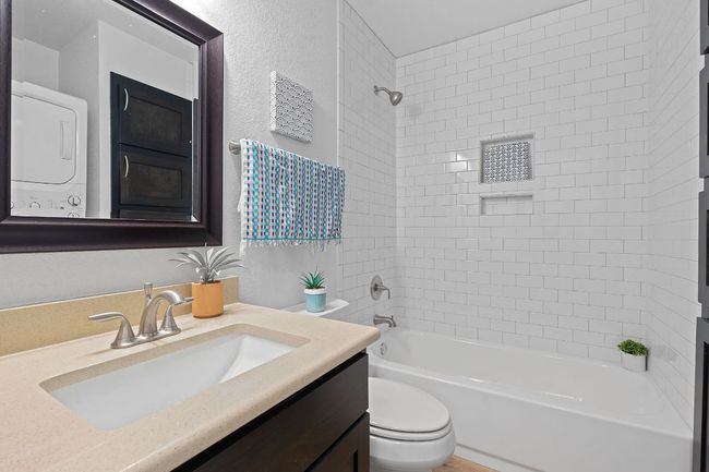 Full bathroom featuring stacked washer and clothes dryer, vanity, a textured wall, and bathing tub / shower combination | Image 17