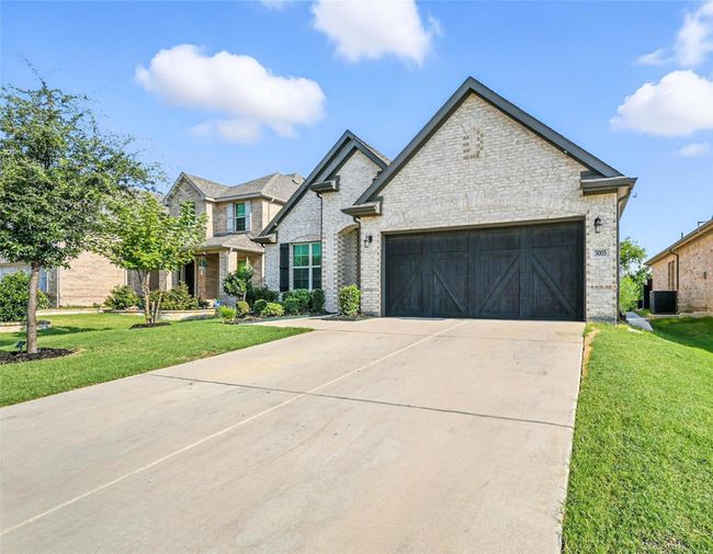 French country inspired facade featuring driveway, an attached garage, a front yard, and brick siding | Image 4