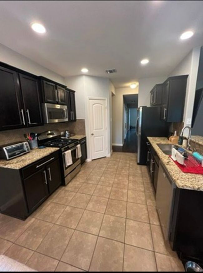 Kitchen with appliances with stainless steel finishes, dark cabinetry, light tile patterned floors, light granite countertops, and backsplash | Image 5