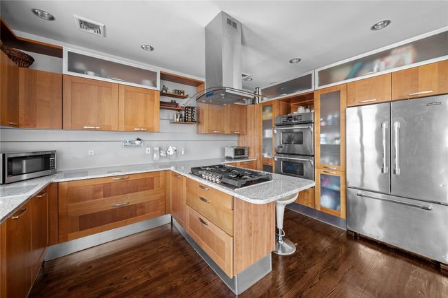 Kitchen featuring dark wood-style floors, stainless steel appliances, island exhaust hood, open shelves, and visible vents | Image 19