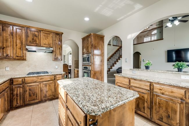 Kitchen featuring appliances with stainless steel finishes, under cabinet range hood, arched walkways, a ceiling fan, and light stone countertops | Image 12