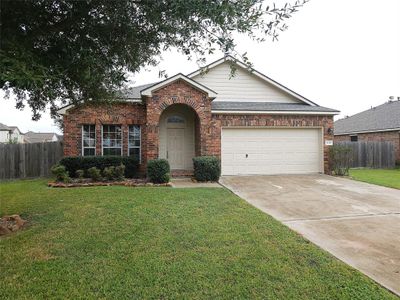 Charming single-story brick home featuring an arched entryway, two-car garage, and neatly landscaped front yard with mature trees. | Image 1