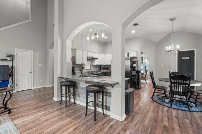 Kitchen featuring a notable chandelier, a breakfast bar, white cabinets, arched walkways, and dark wood-style flooring | Image 6