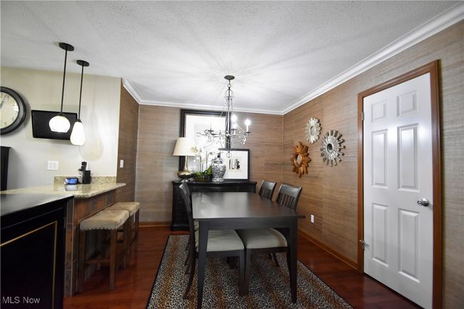 Dining space with dark wood-type flooring, wooden walls, a textured ceiling, a chandelier, and ornamental molding | Image 8