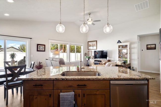 Kitchen featuring stainless steel dishwasher, open floor plan, vaulted ceiling, wood finished floors, and decorative light fixtures | Image 8